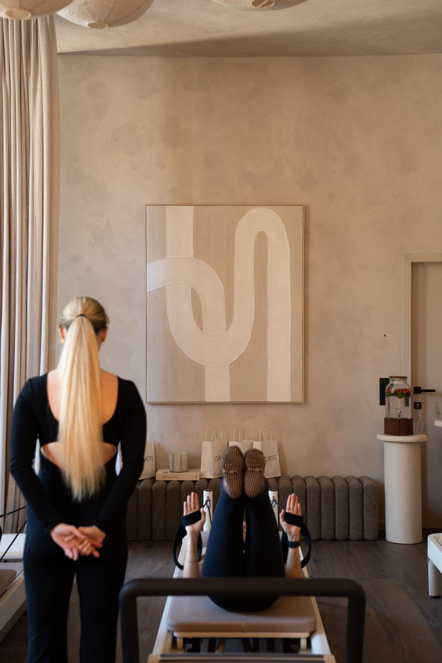 An instructor watching a client on the reformer, in front of the studio's curved artwork